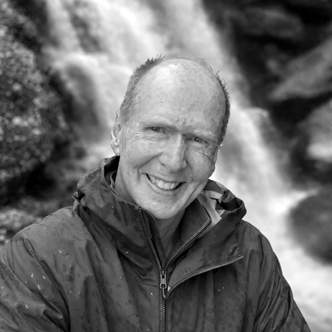 Black-and-white portrait of Charles Skillings, smiling, in front of a waterfall